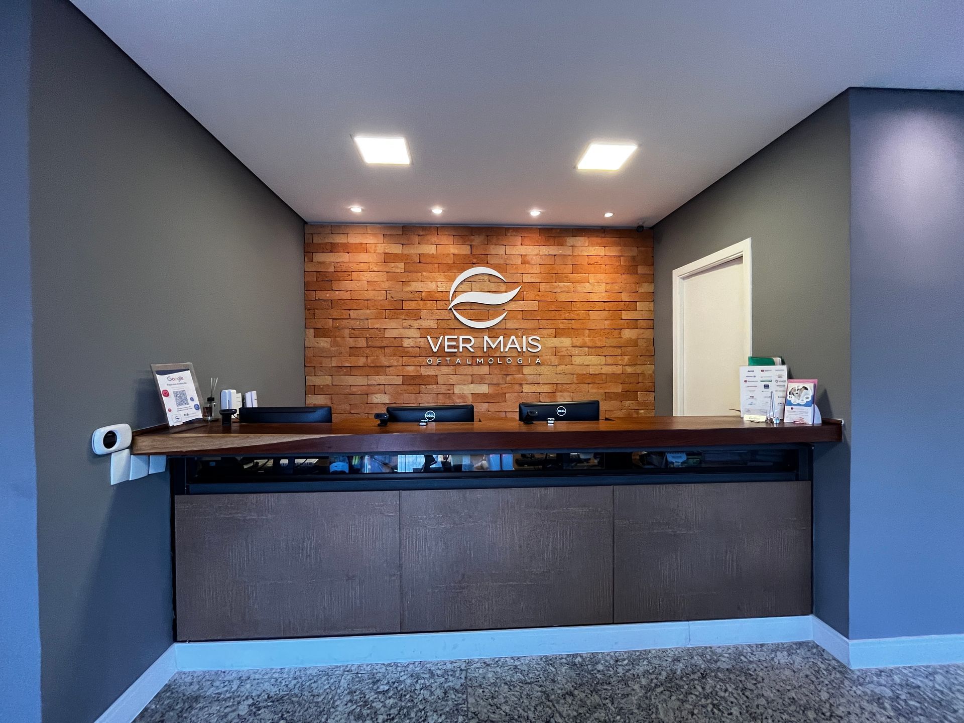 Balcão de recepção com logotipo em uma parede revestida de madeira, em um escritório moderno.