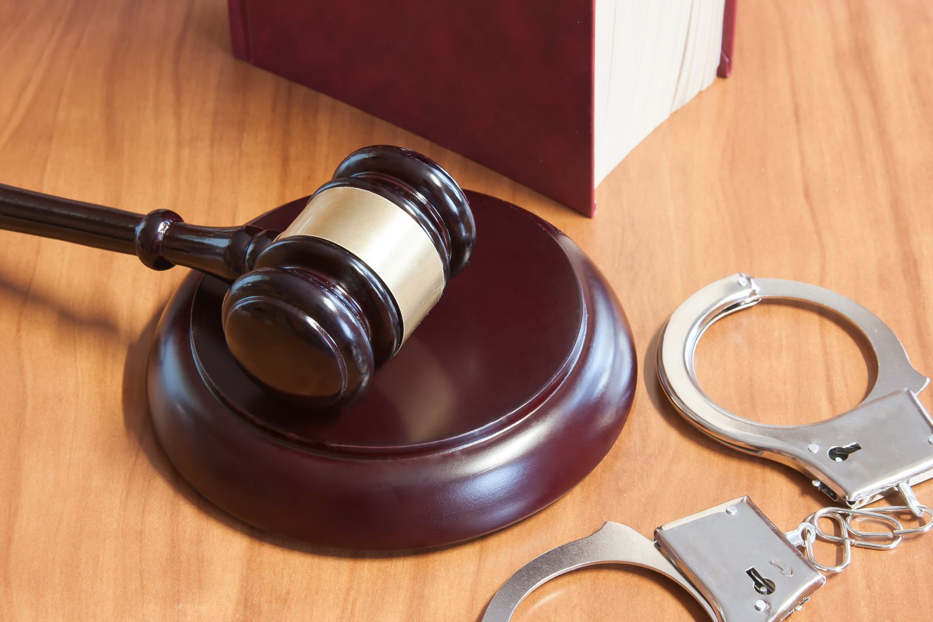 Gavel on block next to open handcuffs and a law book on a wooden surface.
