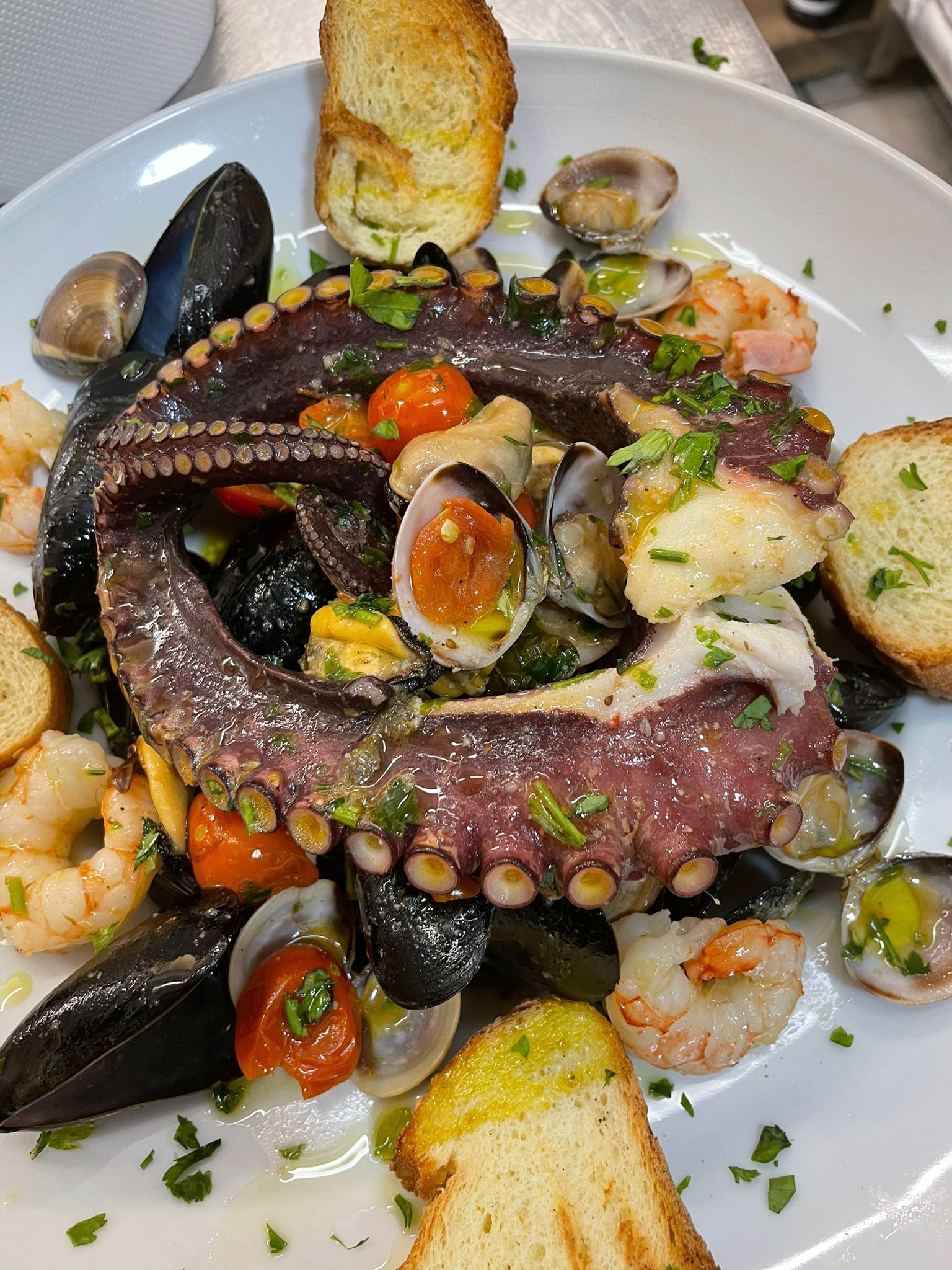 Un piatto di cibo con polpo, gamberi, cozze e pane su un tavolo.