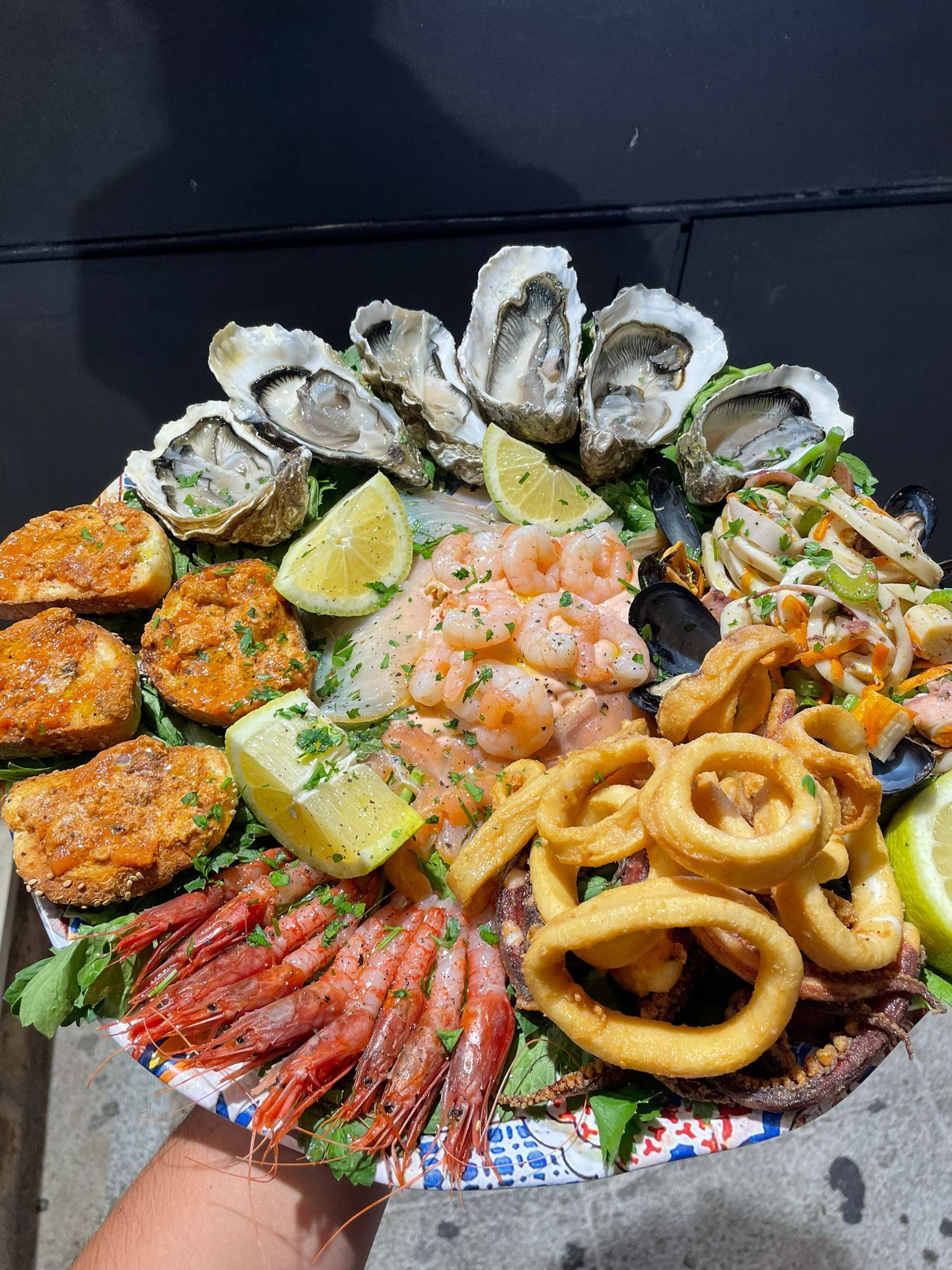 Una persona tiene in mano un piatto di frutti di mare su un piatto di carta.