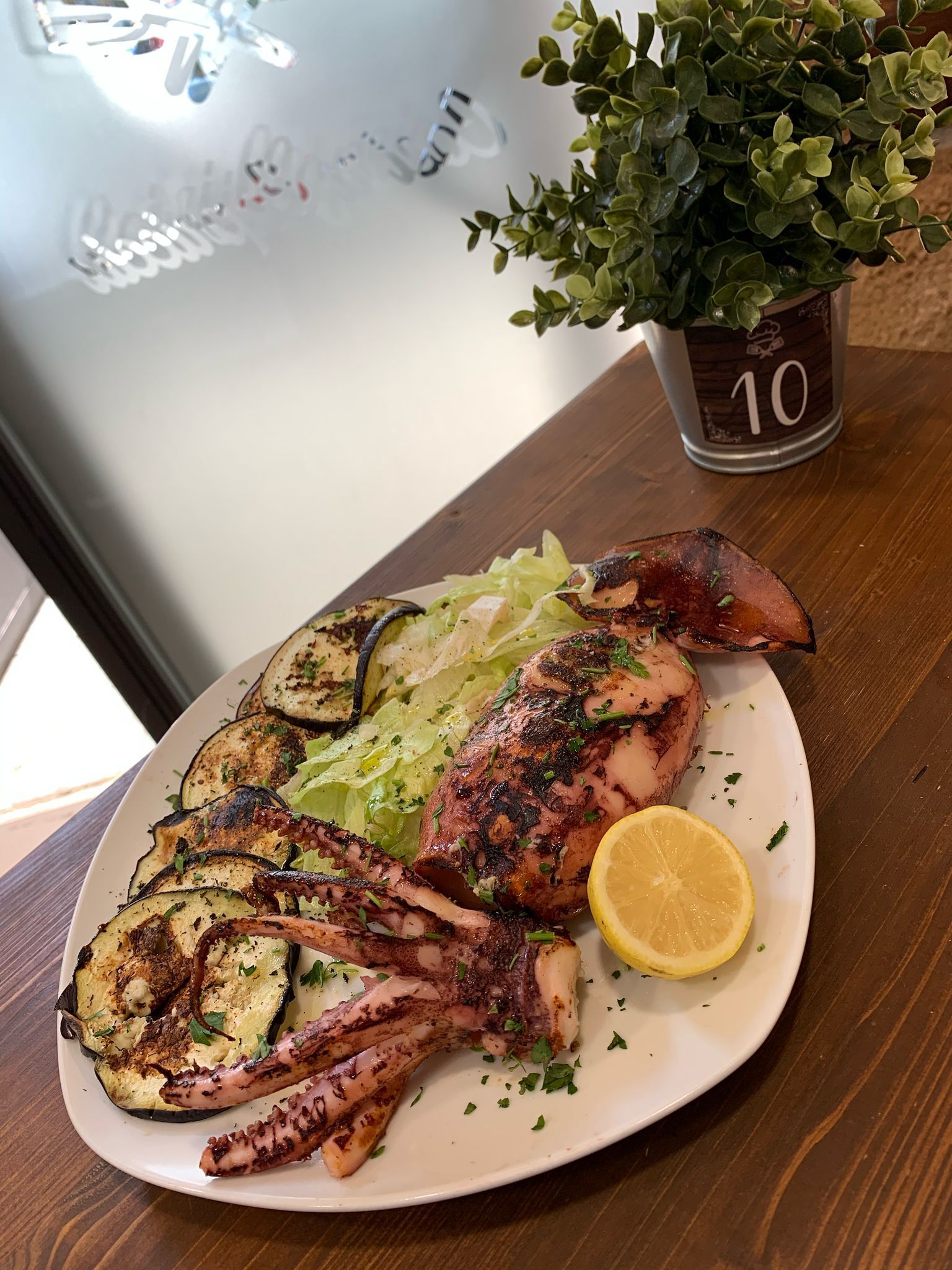 Un piatto bianco con sopra calamari grigliati e verdure su un tavolo di legno.