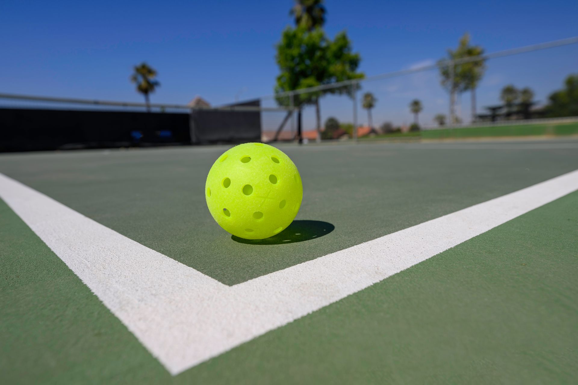 A yellow ball is sitting on the corner of a tennis court.