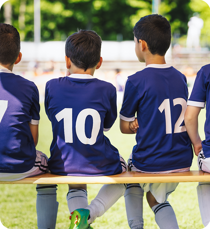 A group of soccer players are sitting on a bench with their backs to the camera.