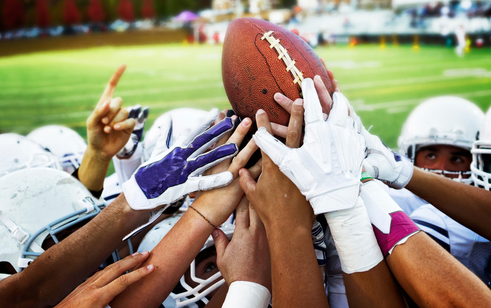 A group of football players are holding a football in their hands.