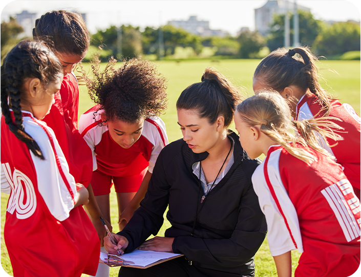 A woman is talking to a group of young girls on a field.