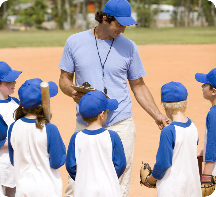 A man in a blue hat is talking to a group of young baseball players