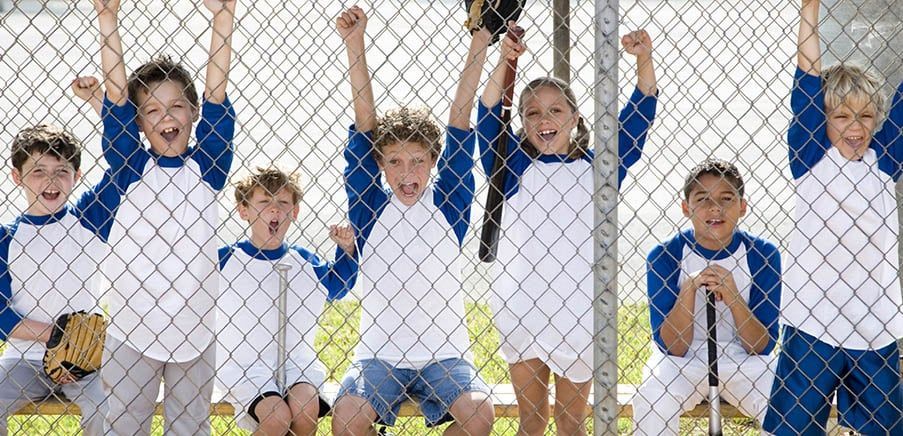 A group of children are sitting on a bench behind a chain link fence.