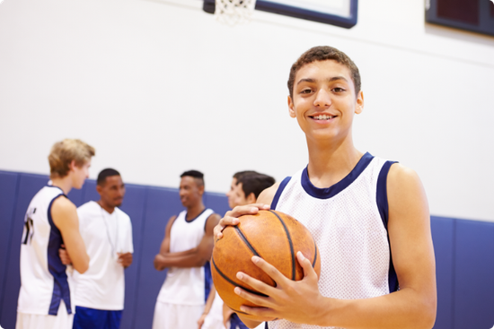 A young man is holding a basketball in a gym.