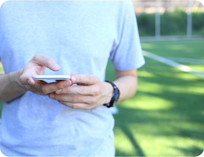 A man in a grey shirt is holding a cell phone in his hands.