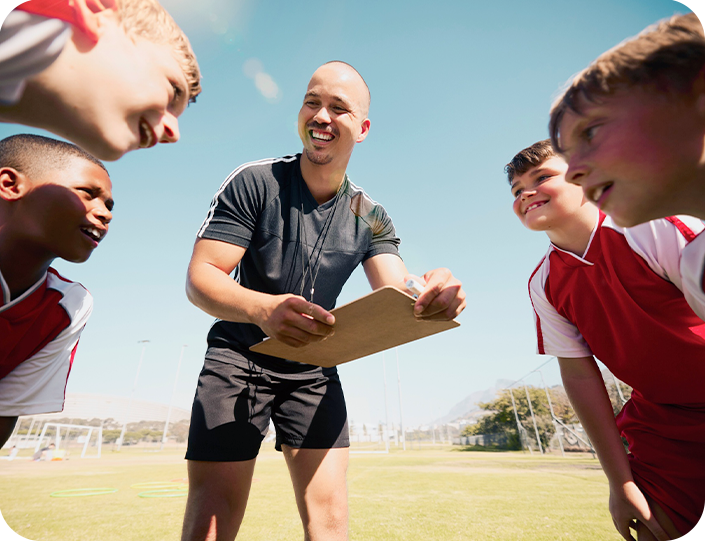 A coach is talking to a group of young boys on a soccer field.