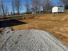 Gravel pile in foreground, excavated earth and trees in the background; daytime.