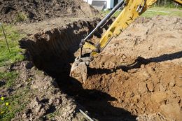 A yellow excavator digging a trench in brown soil on a sunny day.