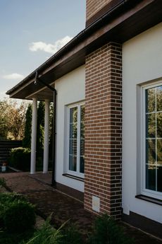 The side of a house with a brick chimney and white windows.