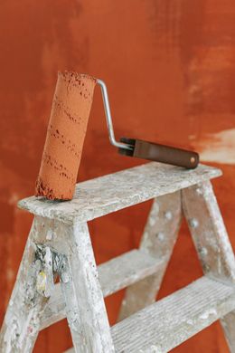 A paint roller is sitting on top of a wooden ladder.