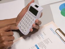 A person is holding a calculator over a clipboard