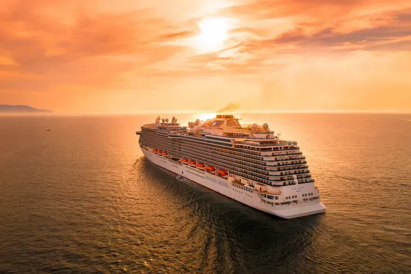 Cruise ship sailing on calm ocean at sunset, orange and golden hues.
