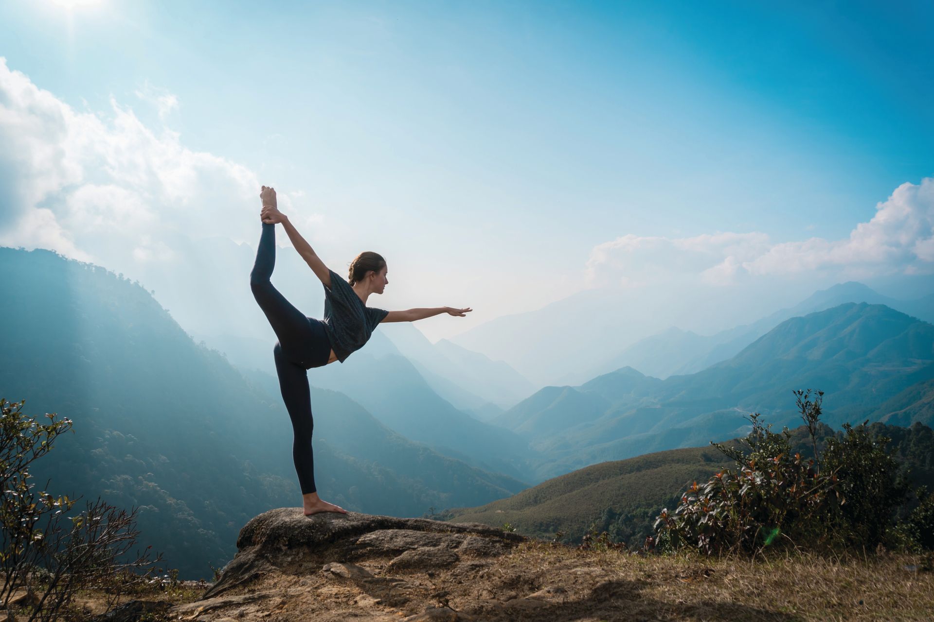 Three women in yoga poses on pink mats in a room with brick walls and large windows.