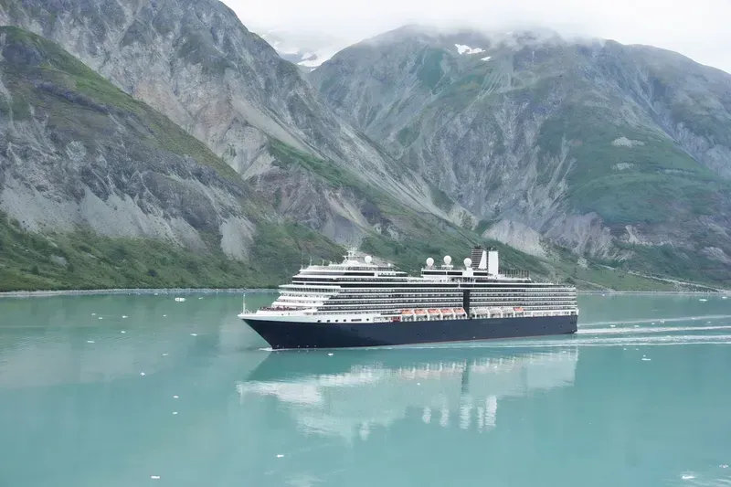 Cruise ship sails on turquoise water, with snow-capped mountains in the background.