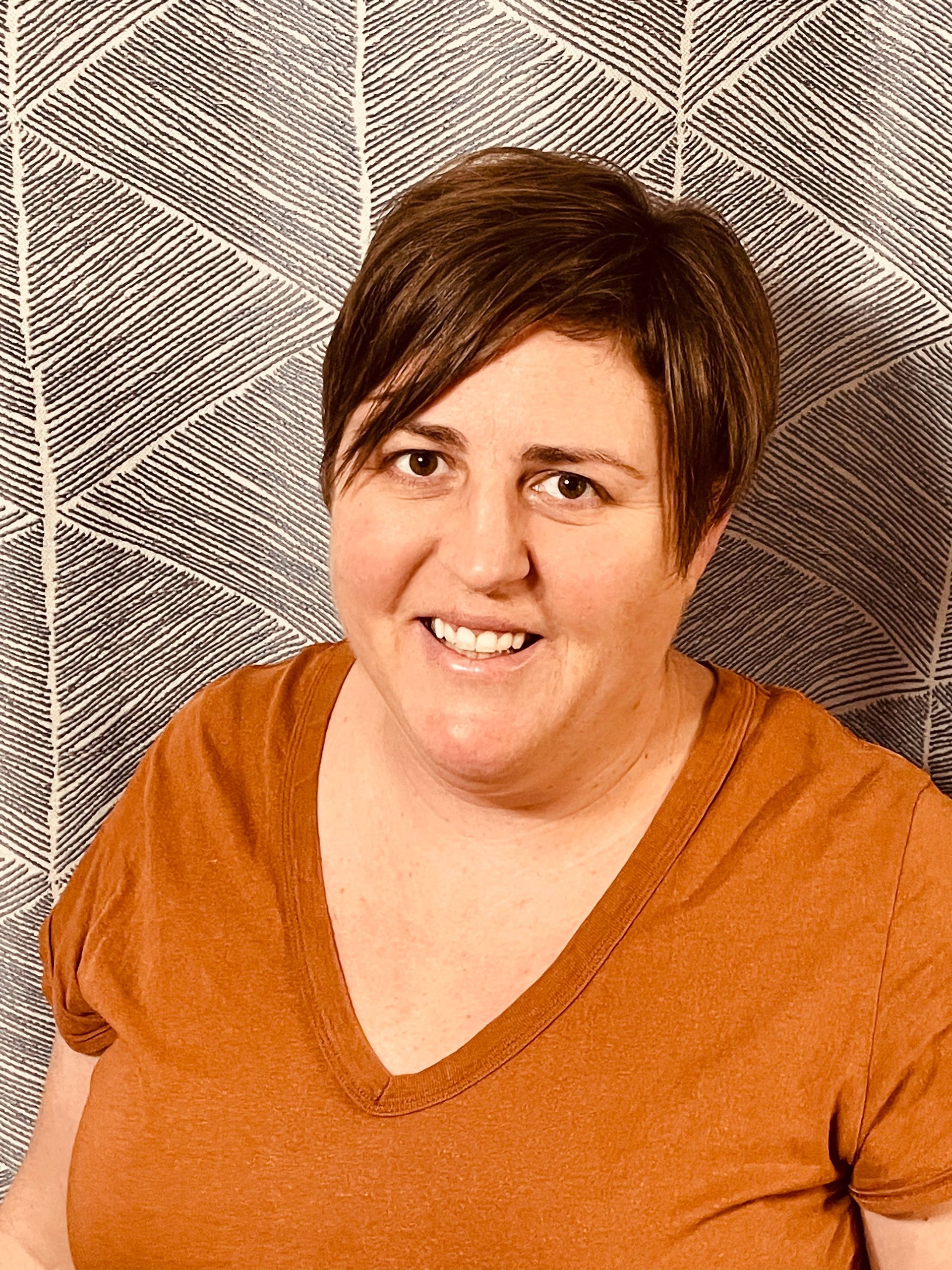 A woman in an orange shirt is smiling for the camera.