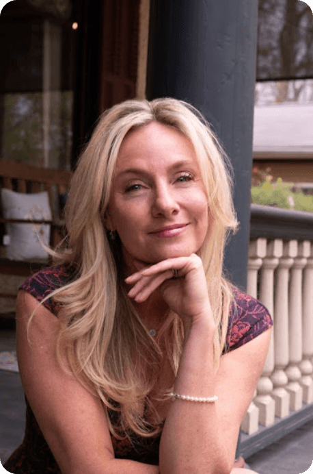 A woman is sitting on a porch with her hand on her chin.