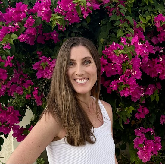 A woman wearing glasses and a blue shirt is standing in front of a brick wall.