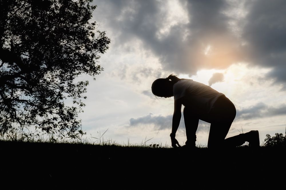 A silhouette of a person kneeling down in the grass.