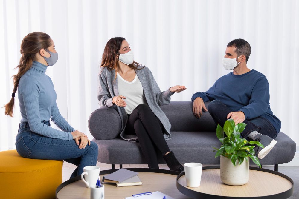 A group of people wearing face masks are sitting on a couch.