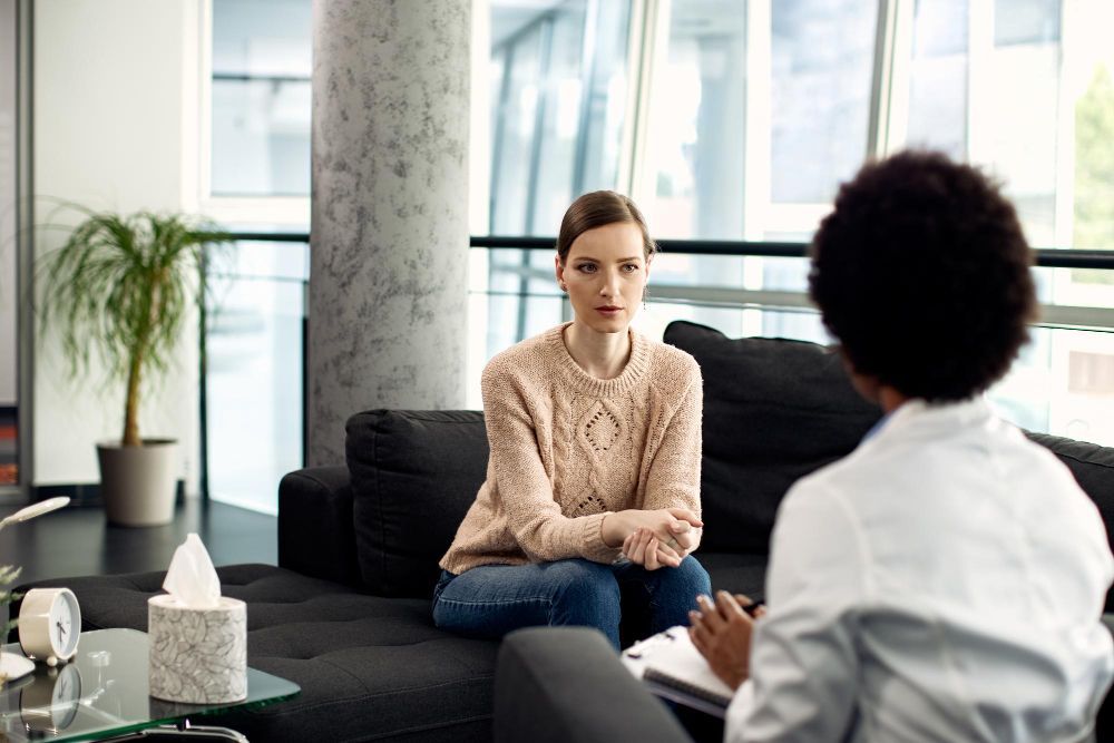 A woman is sitting on a couch talking to a doctor.