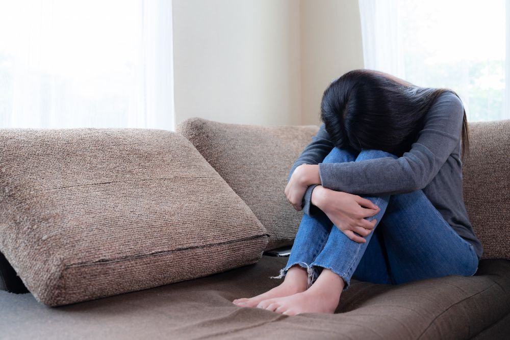 A woman is sitting on a couch with her head down.