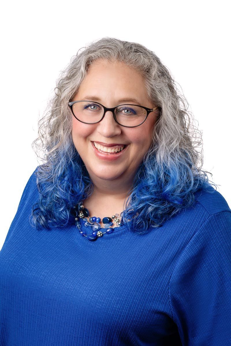 A woman wearing glasses and a blue sweater is smiling for the camera.