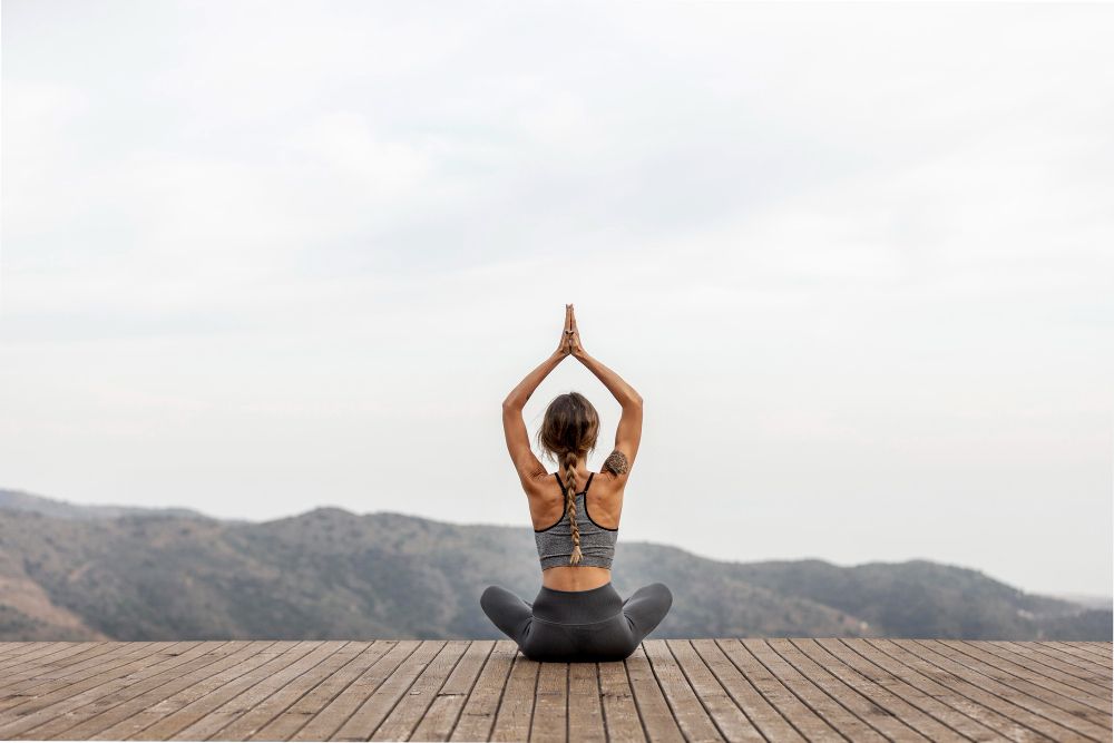 A woman is sitting on a wooden deck doing yoga.