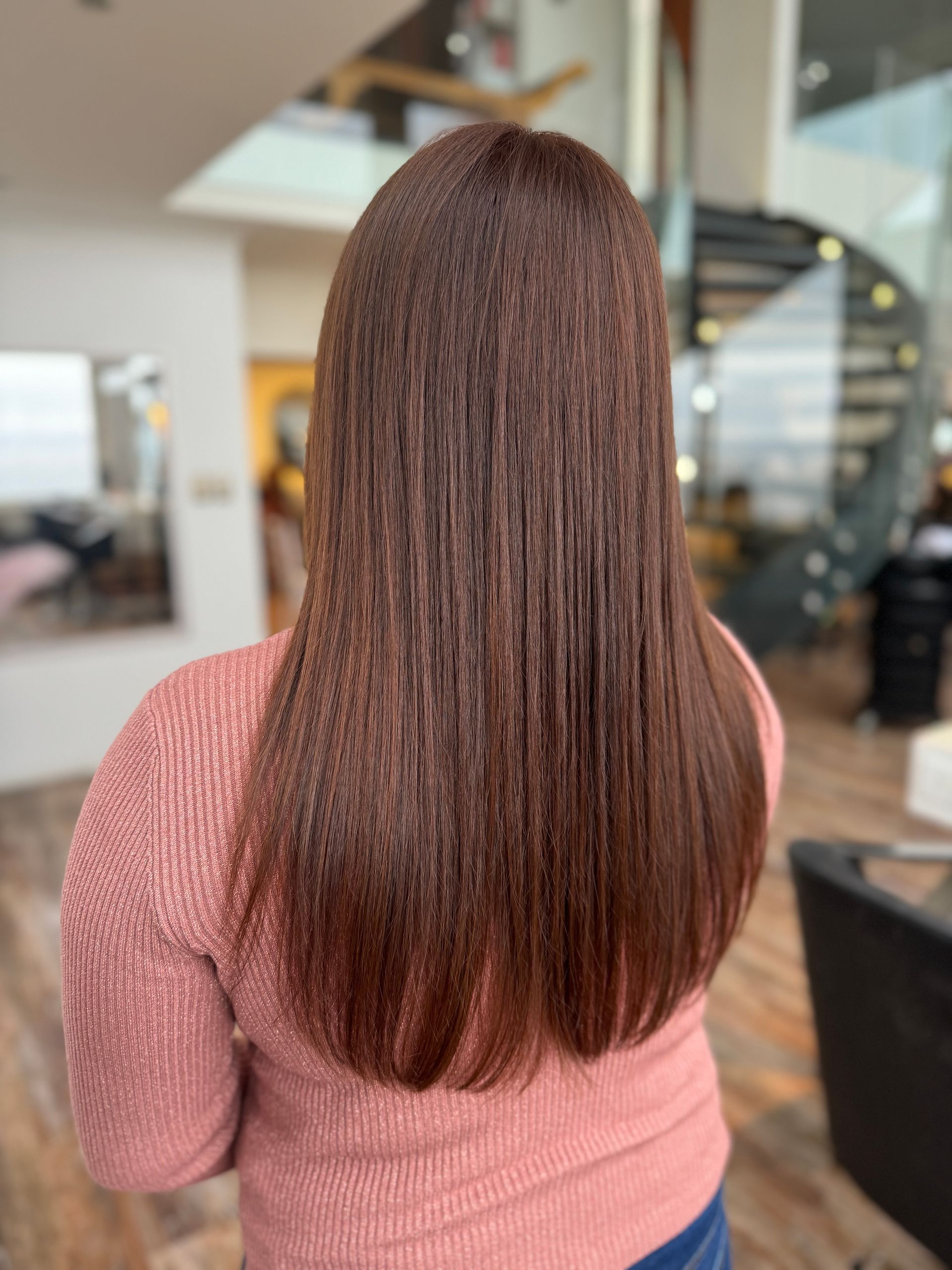 Una mujer con cabello largo y castaño lleva un suéter rosa.
