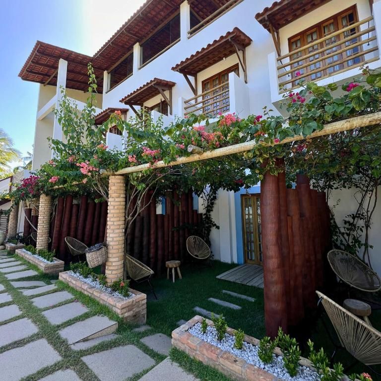 Prédio branco com detalhes em marrom, treliça coberta de flores e cadeiras ao longo de um caminho de pedra.