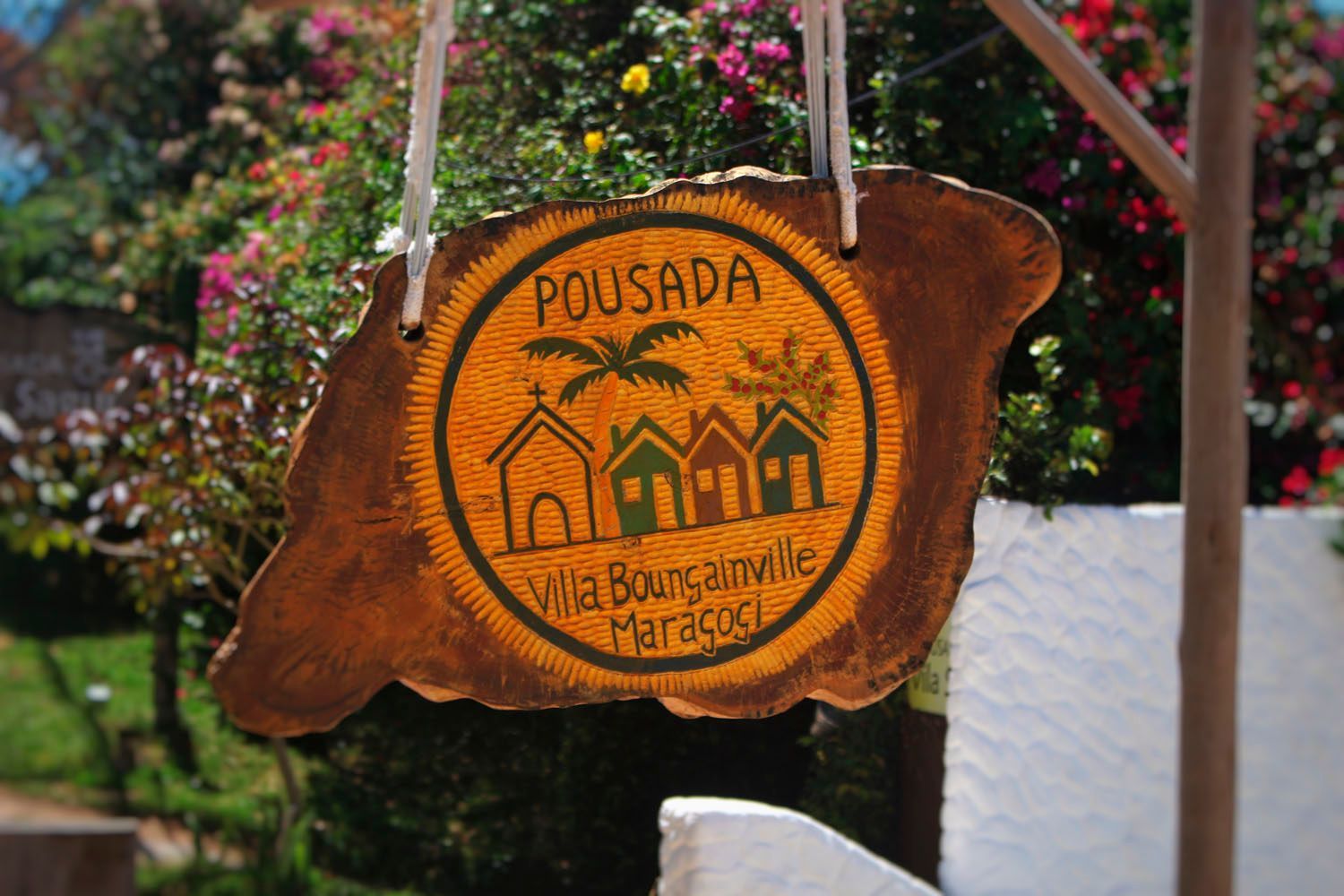 Placa da Pousada Villa Bougainville em Maragogi, Brasil. Placa de madeira com logotipo circular central e letras.