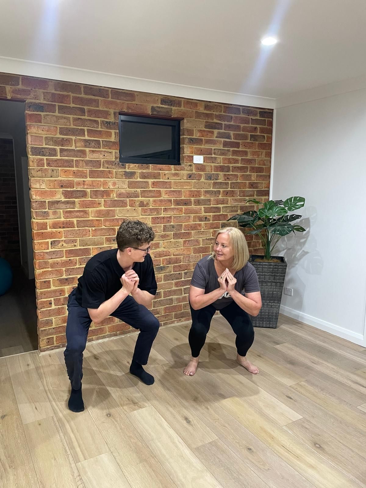 A man and a woman are squatting in a room with a brick wall.