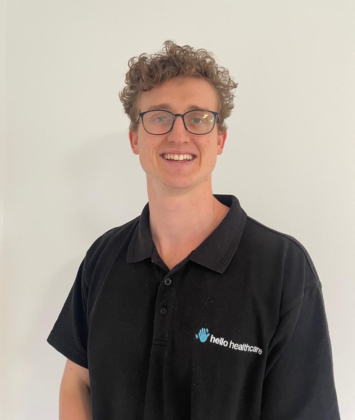 A young man wearing glasses and a black polo shirt is smiling for the camera.