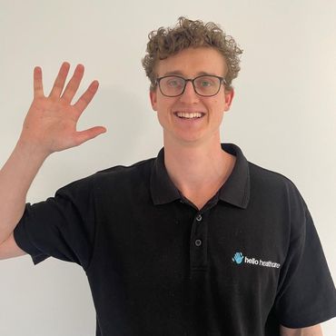 A young man wearing glasses and a black polo shirt is waving his hand