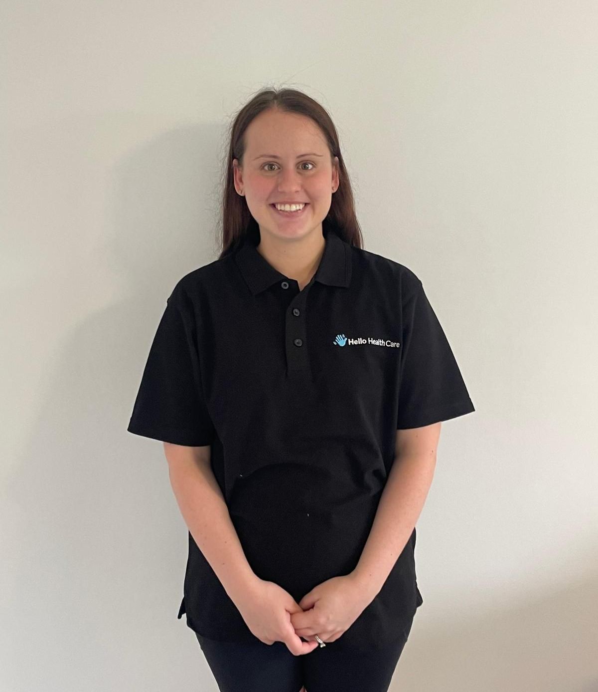 A woman in a black polo shirt is standing in front of a white wall.