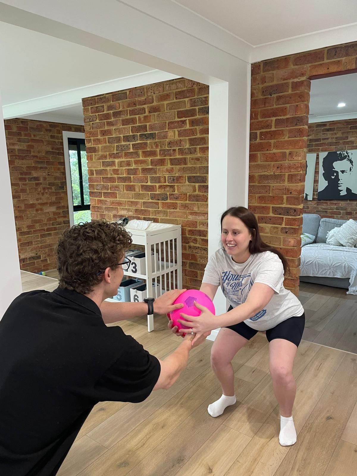 A man and a woman are playing with a pink ball in a living room.