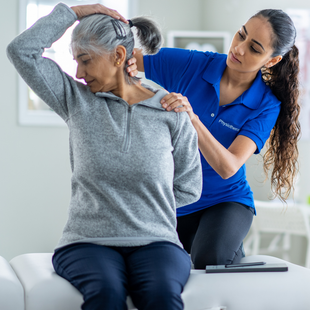 A woman in a blue shirt is helping an older woman stretch her neck.