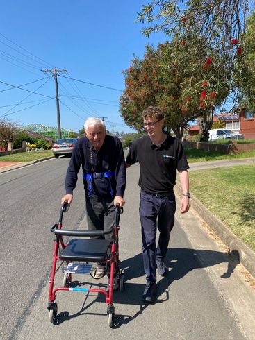 A man is helping an older man with a walker down the street.