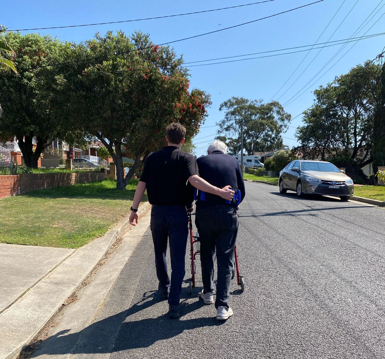 Two men are walking down a street with an older man in a wheelchair