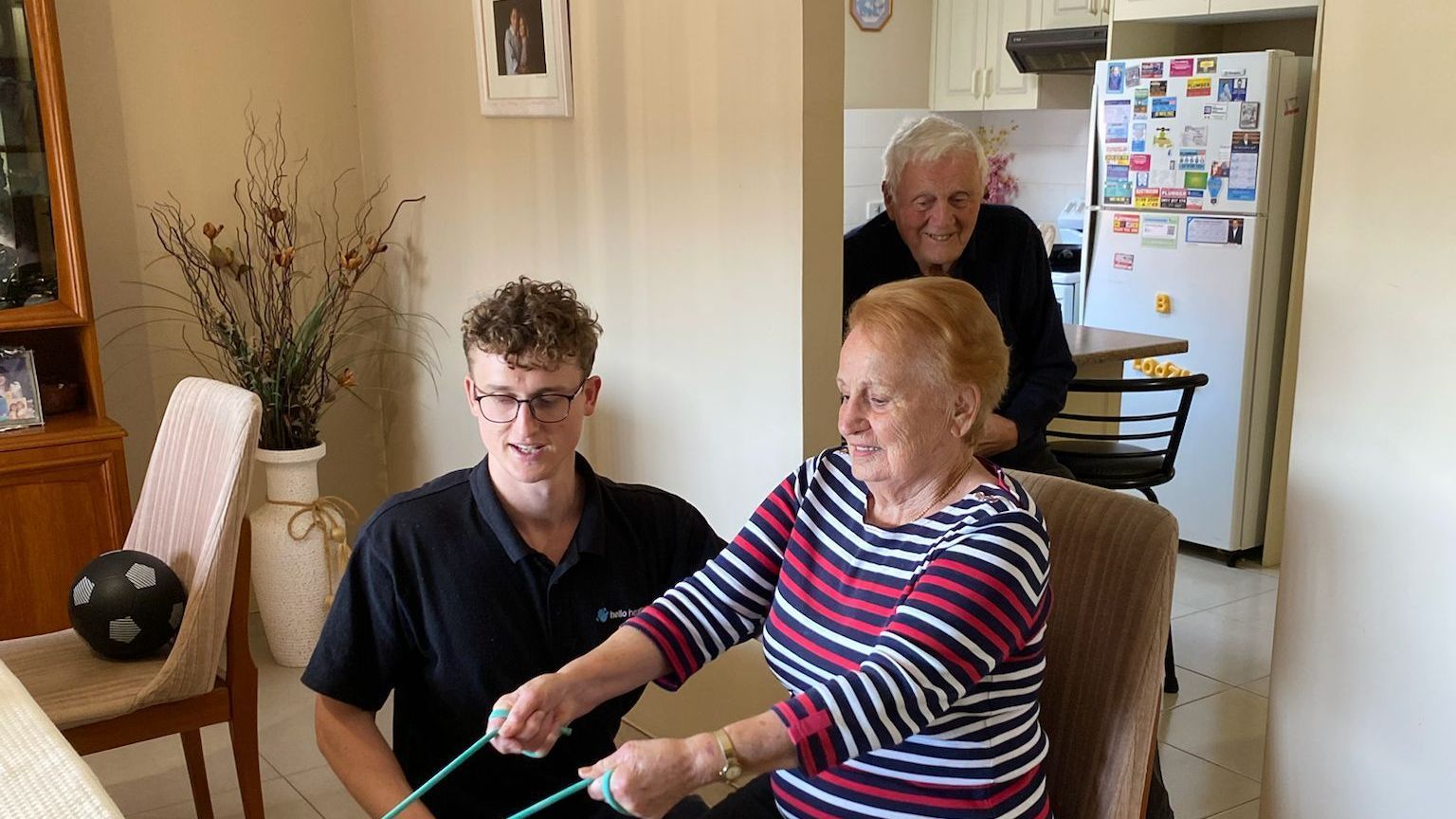 A physiotherapist in Sydney is helping an elderly woman do exercises in a living room.