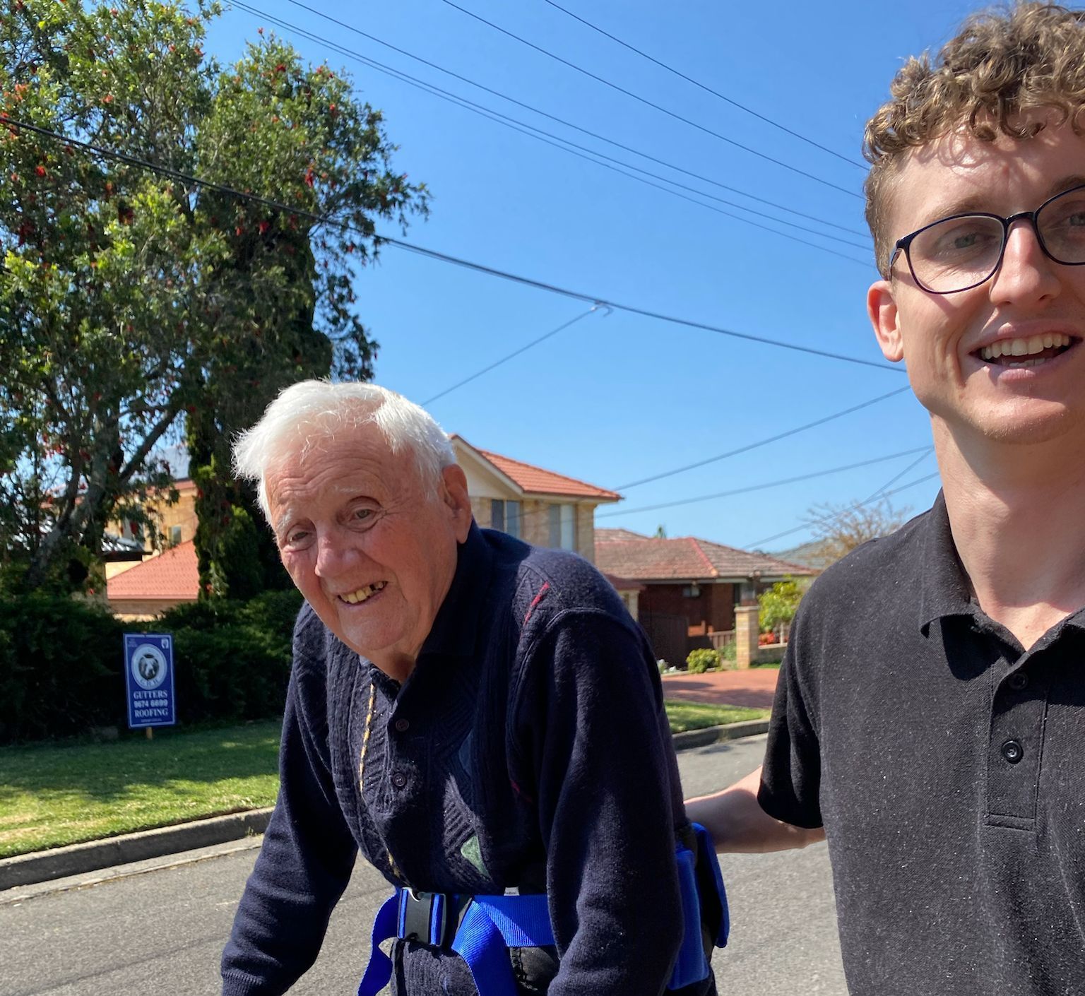 A young man is helping an older man walk down the street.