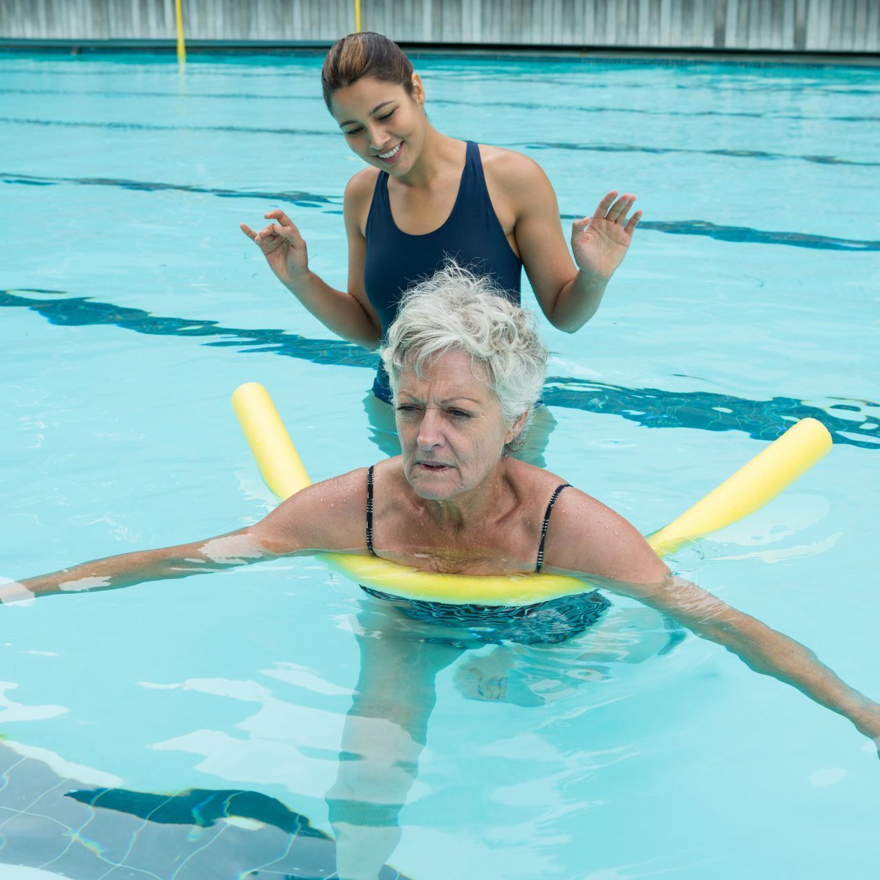 Two people are swimming in a pool with a painting on the wall behind them.