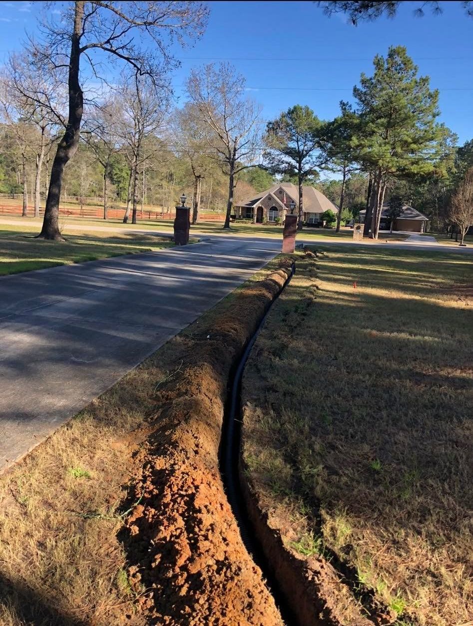 A trench is being dug in the grass next to a road.