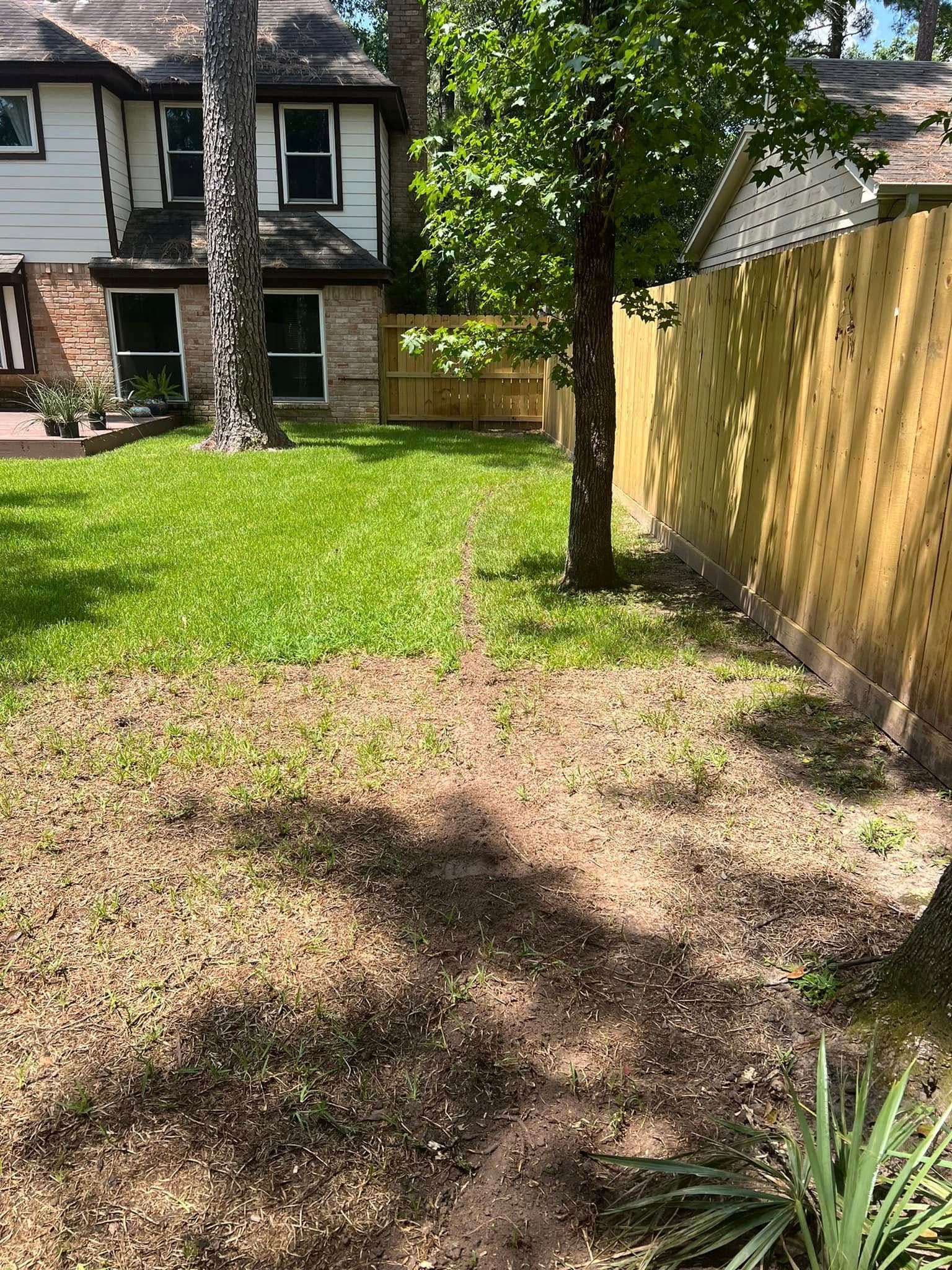 A backyard with a wooden fence and a house in the background.