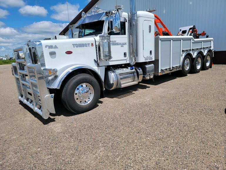 A white tow truck is parked in a gravel lot in front of a building.