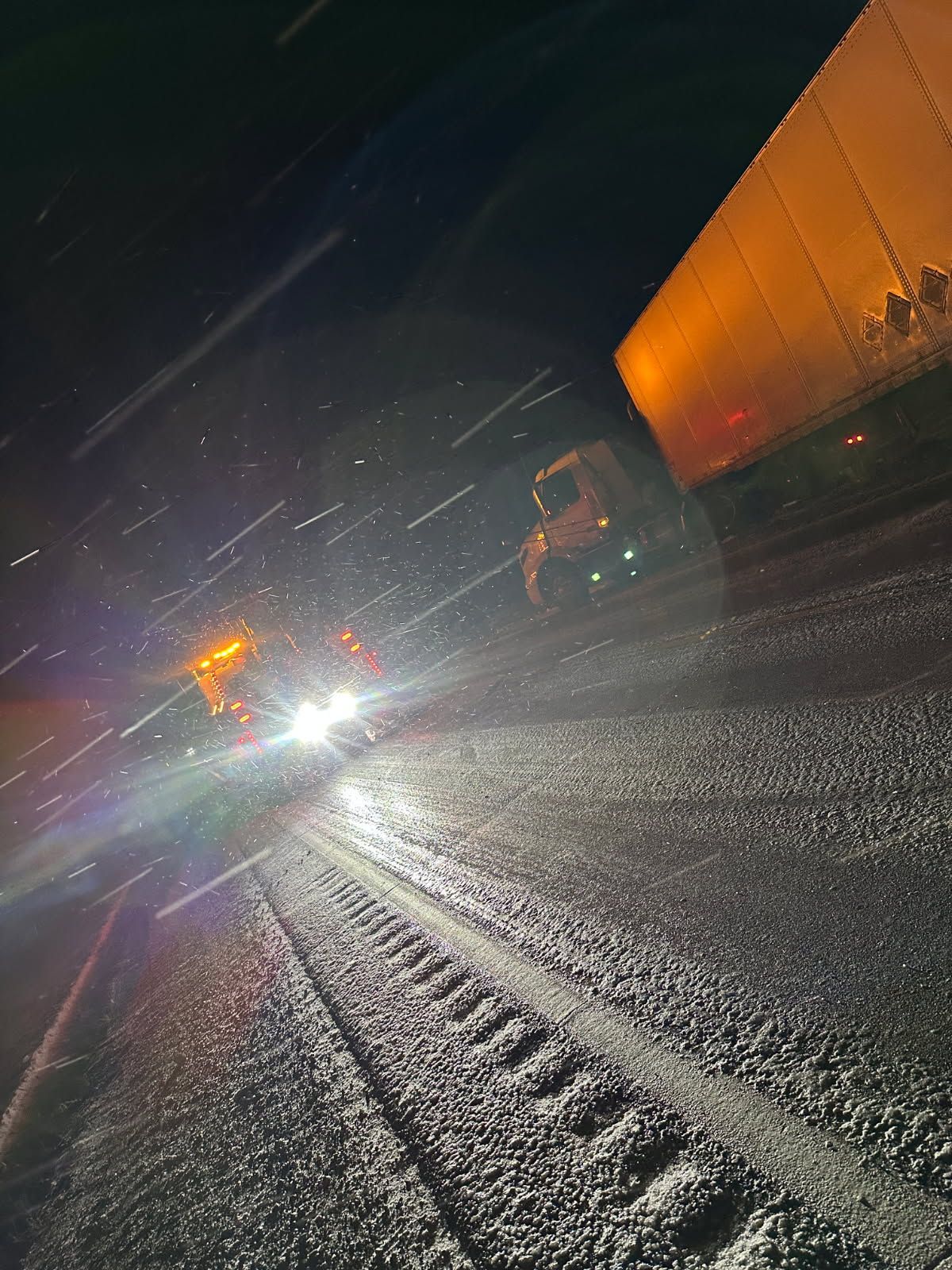 A truck is driving down a snowy road at night