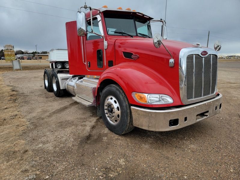 Red Peterbilt semi-truck on dirt ground under cloudy sky.